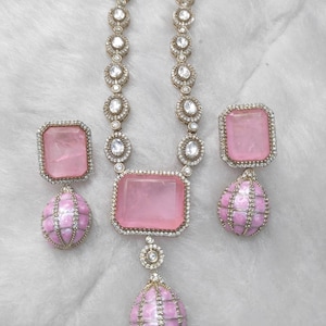 May include: A jewelry set featuring a necklace and earrings. The necklace has a series of clear stones and a large pink square stone pendant. The earrings have pink square stones and pink teardrop-shaped dangles. The set is on a white background.