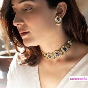 Könnte beinhalten: Goldfarbenes Schmuckset mit einer Halskette und passenden Ohrringen. Die Halskette und die Ohrringe haben ein kreisförmiges Design mit blauen Edelsteinen und weißen Akzenten. Der Text "So beautiful" ist im Bild enthalten.