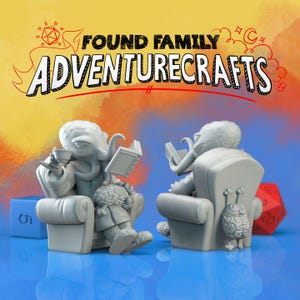 Op de afbeelding: Twee grijze, 3D-geprinte beeldjes van tentakelachtige wezens die in fauteuils zitten. De beeldjes houden boeken vast en zijn omringd door dobbelstenen.