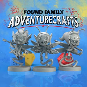 May include: Three grey painted miniature figurines of fairy-like creatures with wings, each standing on a round base. The figures are part of a set called "Found Family Adventurecrafts".