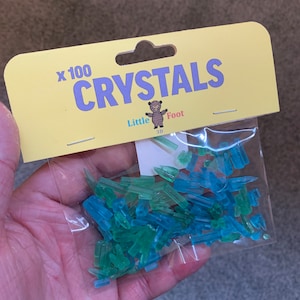Può includere: Un sacchetto di 100 piccoli cristalli di plastica trasparente in tonalità di blu e verde. Il sacchetto è etichettato "x100 CRYSTALS" e "Little Foot 3D".