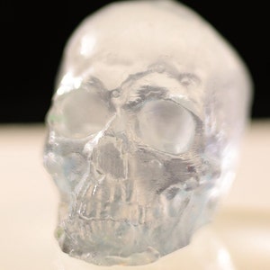 Könnte beinhalten: Eine durchsichtige Glasschädelskulptur mit detaillierten Merkmalen. Der Schädel ist durchscheinend und hat einen leicht bläulichen Farbton.