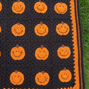 May include: A black crocheted blanket featuring smiling orange pumpkin appliques. The blanket has an orange border with a decorative edge. The pumpkins have brown stems and black stitched smiles. The blanket is likely handmade.