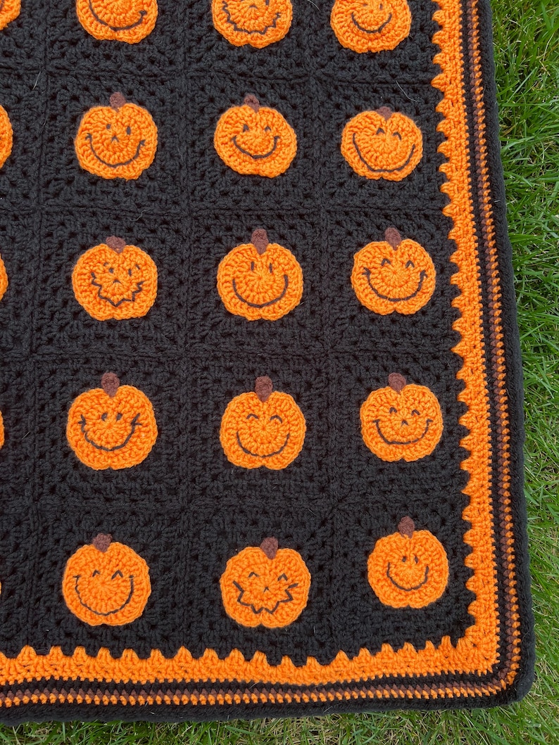 May include: A black crocheted blanket featuring smiling orange pumpkin appliques. The blanket has an orange border with a decorative edge. The pumpkins have brown stems and black stitched smiles. The blanket is likely handmade.