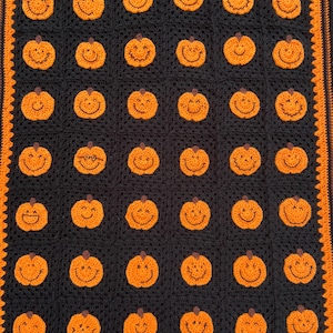 May include: A black and orange crocheted blanket featuring a repeating pattern of smiling orange pumpkins. The blanket has an orange border and is perfect for Halloween or autumn decor.