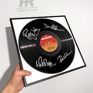 May include: Framed black vinyl record with signatures. The record features a Columbia label and the text "PINK FLOYD COMFORTABLY NUMB". The frame is black and the background is white. The text "PHONIC RAPTURE" is in the upper left corner.