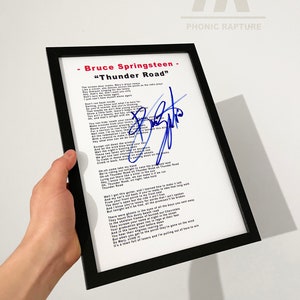 Puede incluir: Impresión enmarcada de la letra de "Thunder Road" de Bruce Springsteen, con una firma azul. El marco negro rodea un fondo blanco con el título y la letra de la canción. El logotipo de Phonic Rapture es visible en la esquina superior derecha.