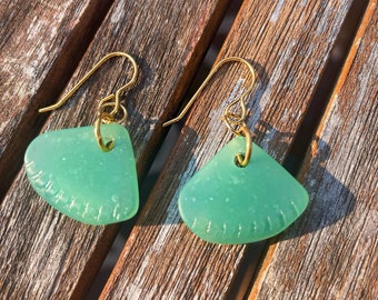 May include: A pair of green glass earrings with gold hooks. The earrings are shaped like a fan and have a textured surface.