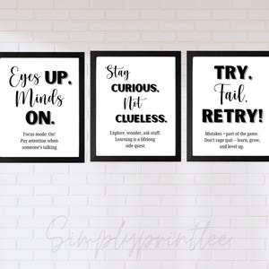 May include: Three framed motivational prints with black frames and white backgrounds. The prints feature black text with phrases like "Eyes Up. Minds On.", "Stay Curious. Not Clueless.", and "Try. Fail. Retry!" The prints are displayed on a white brick wall.