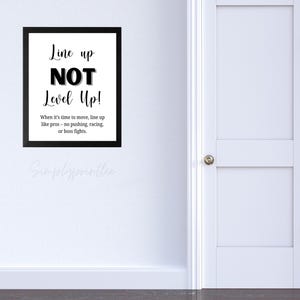 May include: A framed black and white print with the text "Line up NOT Level Up!". The print includes the text "When it's time to move, line up like pros - no pushing, racing, or boss fights."