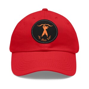 May include: Red baseball cap with a black and white circular patch featuring a silhouette of a person holding a bow and arrow. The patch has the text "Jai Shiv Ram" in orange.