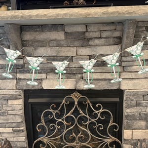 May include: A green and white paper garland with martini glasses hanging from a string. The garland is hanging above a fireplace.