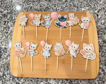 Op de afbeelding: Een set van 12 cupcake-toppers met schattige cartoon-kittens met roze ballonnen, harten en bloemen. De toppers zijn gedrukt op stevig papier en bevestigd aan houten stokjes.