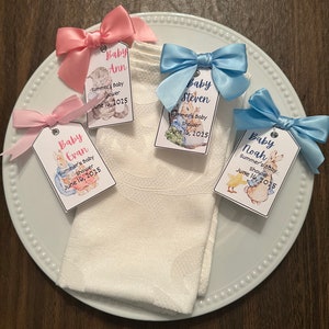 May include: Four baby shower favor tags with pink and blue bows. Each tag features a different baby's name, "Baby Ann", "Baby Evan", "Baby Steven", and "Baby Noah". The tags also include the text "Summer's Baby Shower" and the date "June 16, 2025".
