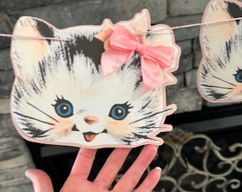 May include: A white and black cat with pink bow, paper cutout for a party banner or garland.