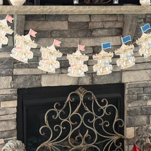 May include: A white and gold carousel horse banner with blue and pink flags hanging above a fireplace.