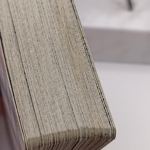 Puede incluir: Primer plano de una baraja de cartas con un aspecto desgastado y texturizado. Los bordes de las cartas son visibles, mostrando capas individuales. Las cartas tienen un color claro y neutro, lo que sugiere edad o uso. La baraja est&aacute; ligeramente curvada.