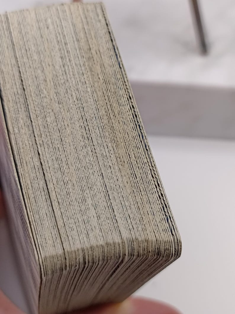 Puede incluir: Primer plano de una baraja de cartas con un aspecto desgastado y texturizado. Los bordes de las cartas son visibles, mostrando capas individuales. Las cartas tienen un color claro y neutro, lo que sugiere edad o uso. La baraja est&aacute; ligeramente curvada.