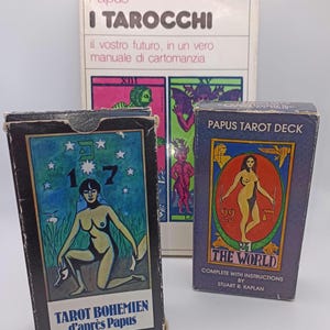 Puede incluir: Un conjunto de tres artículos de tarot que incluye un libro titulado I TAROCCHI de Papus, una caja negra etiquetada TAROT BOHEMIEN d'après Papus con una figura bajo estrellas, y una caja azul PAPUS TAROT DECK THE WORLD con una figura central.