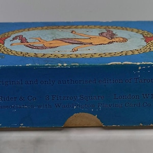 Puede incluir: Una caja de cartas de tarot azul vintage con las palabras "CARDS" y "TAROT". La caja presenta una ilustraci&oacute;n de una figura en un &oacute;valo dorado. El texto en la caja dice "The original and only authorised edition of Tarot Cards."
