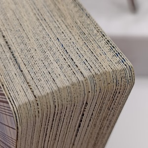Puede incluir: Primer plano de una baraja de cartas con un aspecto texturizado y envejecido. Los bordes de las cartas son visibles, mostrando un efecto en capas con un color beige claro y l&iacute;neas oscuras. La esquina de la baraja revela un dise&ntilde;o estampado.