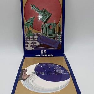 May include: Two tarot cards with blue borders and gold backgrounds. The top card has the text "IL GIUDIZIO" and a red circle with a green architectural design. The bottom card has the text "LA LUNA" and a crescent moon design.