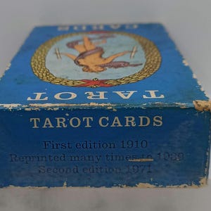 Puede incluir: Una caja de cartas del tarot azul vintage con la palabra "TAROT" en la parte superior. La caja presenta una ilustraci&oacute;n y el texto "TAROT CARDS, First edition 1910, Reprinted many times to 1989, Second edition 1971."