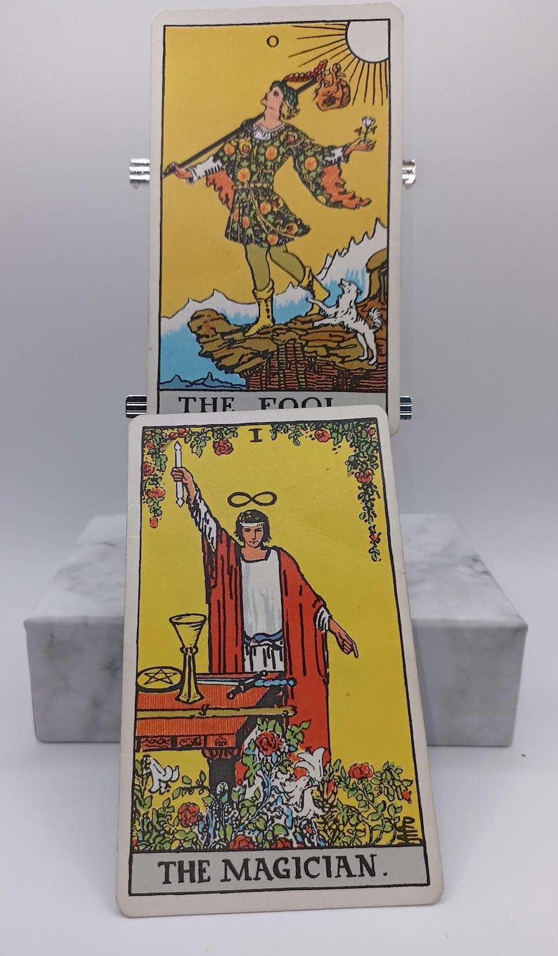 Puede incluir: Se muestran dos cartas del tarot. La carta superior es "El Loco", que representa una figura con un bast&oacute;n y una bolsa. La carta inferior es "El Mago", que muestra a una persona con t&uacute;nicas rojas sosteniendo una varita. Ambas cartas tienen fondos amarillos.