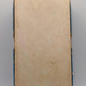 Puede incluir: Una caja rectangular vintage con tapa de color beige claro y ribete azul. La caja muestra signos de antig&uuml;edad, con decoloraci&oacute;n y desgaste en la superficie de papel. Los bordes de la caja est&aacute;n ligeramente desgastados.