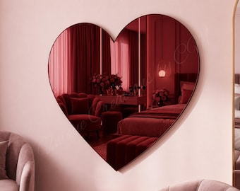 May include: A heart-shaped wall mirror with a dark red tinted reflective surface. The mirror features a thin, dark frame and reflects a room interior with red furniture, including a chair, a bed, and a table with a floral arrangement.