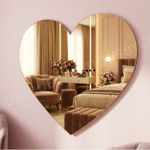 May include: A heart-shaped wall mirror with a gold frame. The mirror reflects a bedroom scene with a bed, vanity, and seating area. The room is decorated in shades of pink and beige, creating a soft and elegant atmosphere. A decorative piece for home decor.