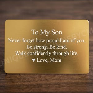 May include: A gold-colored rectangular plaque with rounded corners. The text "To My Son" is at the top, followed by an inspirational message and "Love, Mom" at the bottom. The plaque is set against a dark wood background.