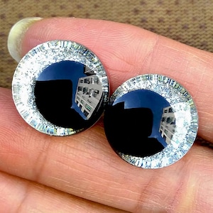 May include: A pair of black and silver round buttons with a glittery silver rim. The buttons are reflective and show a blurry reflection of a building.