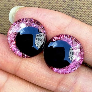 May include: Two black plastic eyes with a pink glitter rim. The eyes are round and have a reflective surface.
