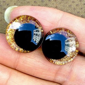 May include: Two large, round, black plastic eyes with a gold glitter rim. The eyes are on a hand.