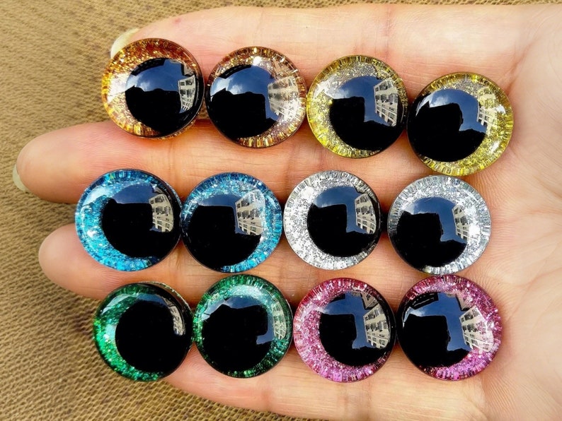May include: Assortment of 10 colorful plastic googly eyes with glitter accents. The eyes are black in the center and have a variety of colors around the edges, including gold, silver, blue, green, and pink.