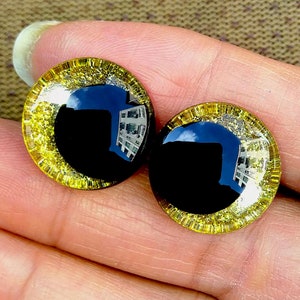 May include: Two black plastic eyes with a gold glitter rim. The eyes are round and have a reflective surface.