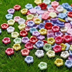 Peut inclure: Un assortiment de boutons en forme de fleurs de couleurs vives : rouge, rose, jaune, vert, bleu et violet. Les boutons sont dispersés sur de l'herbe verte, créant une scène joyeuse et colorée. Chaque bouton a deux trous.