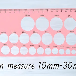 May include: Pink plastic ruler with a series of circles of different sizes, ranging from 10mm to 30mm in diameter. The ruler has a scale marked in millimeters.