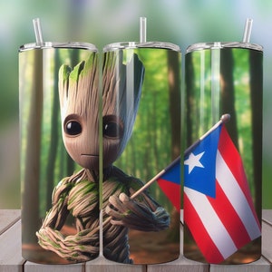 Puede incluir: Un vaso de acero inoxidable con un diseño verde, marrón y rojo. El diseño presenta un personaje de dibujos animados sosteniendo una bandera con una estrella blanca y rayas rojas y blancas. El fondo es una imagen borrosa de un bosque.