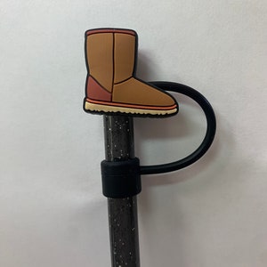 May include: A brown boot charm with a black elastic band. The charm is attached to a black and silver glitter pen.