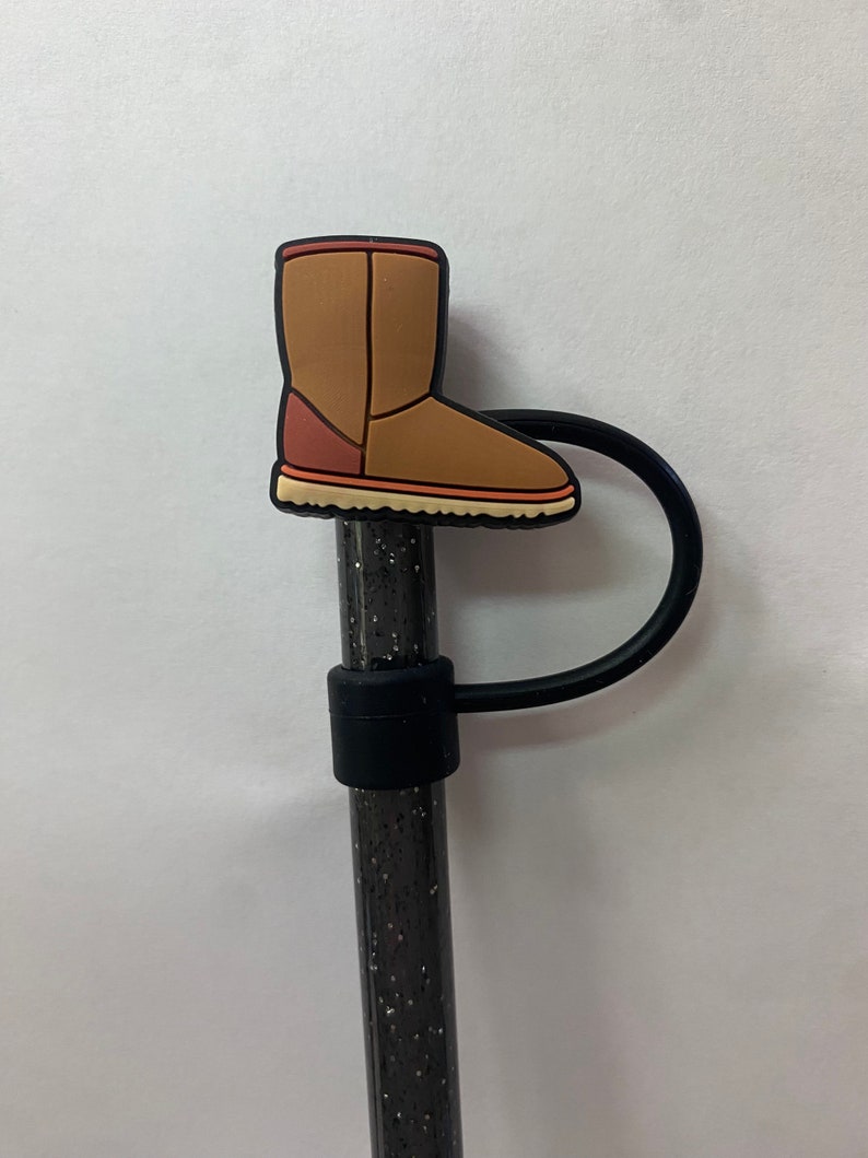 May include: A brown boot charm with a black elastic band. The charm is attached to a black and silver glitter pen.