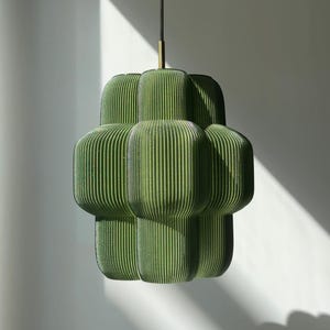 Puede incluir: Lámpara colgante verde con diseño acanalado. La lámpara tiene un diseño único y en capas con secciones verticales redondeadas. Cuelga de un cable negro con un acento dorado.