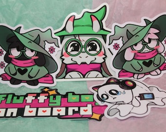 May include: A collection of cartoon stickers featuring characters with green hats, glasses, and pink scarves. One sticker reads "Fluffy boi on board" in green and pink. A white cartoon ghost-like character with headphones and a phone is also included.