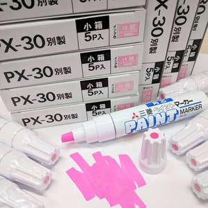 May include: White PX-30 paint markers with pink ink are displayed, along with boxes of the same markers. The boxes have Japanese text and pink labels. A pink ink swatch and a marker cap are also visible.