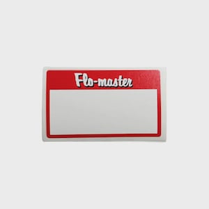 May include: A rectangular sticker with a red border and a white interior. The top of the sticker has the words "Flo-master" in a white, stylized font with a black outline. The sticker is on a light gray background.