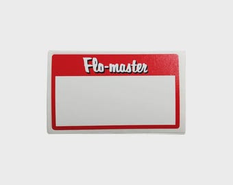Puede incluir: Una pegatina rectangular con borde rojo e interior blanco. La parte superior de la pegatina tiene las palabras "Flo-master" en una fuente blanca estilizada con un contorno negro. La pegatina está sobre un fondo gris claro.