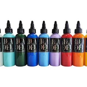 May include: Ten bottles of tattoo ink in various colours, including white, turquoise, green, blue, light blue, lavender, red, orange, and yellow. Each bottle has a black label with the text "ILA DYE" in white.