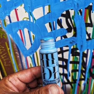 May include: A blue paint bottle with a black label that says "HAND-MIXED SINCE 1997 PERMANENTRADER SUPERIOR COLOR".