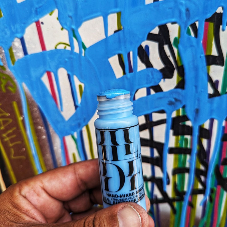 May include: A blue paint bottle with a black label that says "HAND-MIXED SINCE 1997 PERMANENTRADER SUPERIOR COLOR".